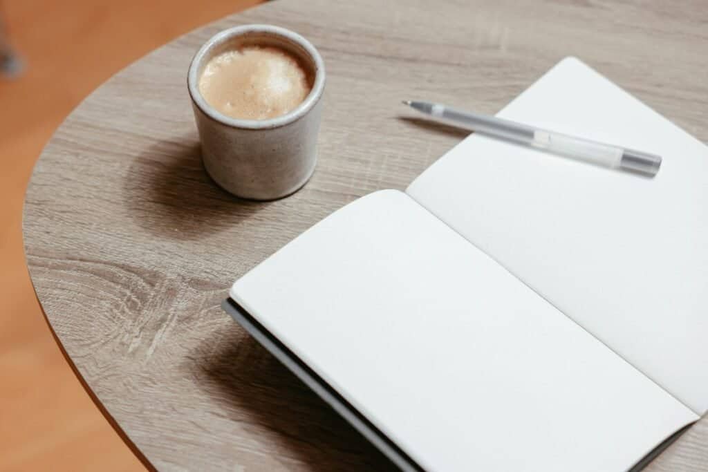 taccuino aperto con penna e tazza di caffè per pianificare le attività e sviluppare autodisciplina