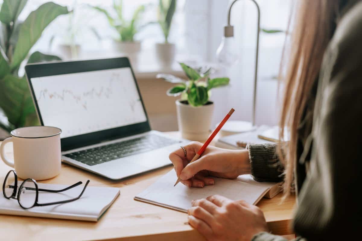 persona che pianifica le attività scrivendo su un taccuino mentre lavora al laptop per sviluppare autodisciplina e costanza