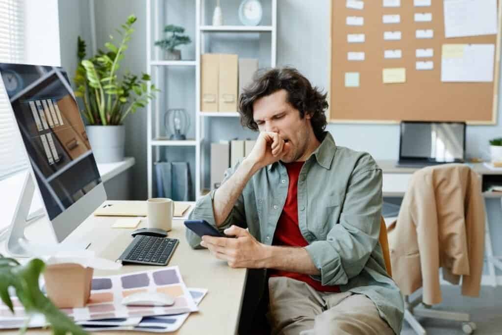 uomo distratto dal telefono mentre lavora procrastinazione