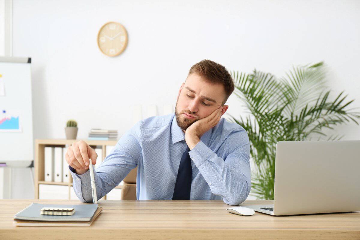 Uomo annoiato alla scrivania mentre procrastina durante il lavoro
