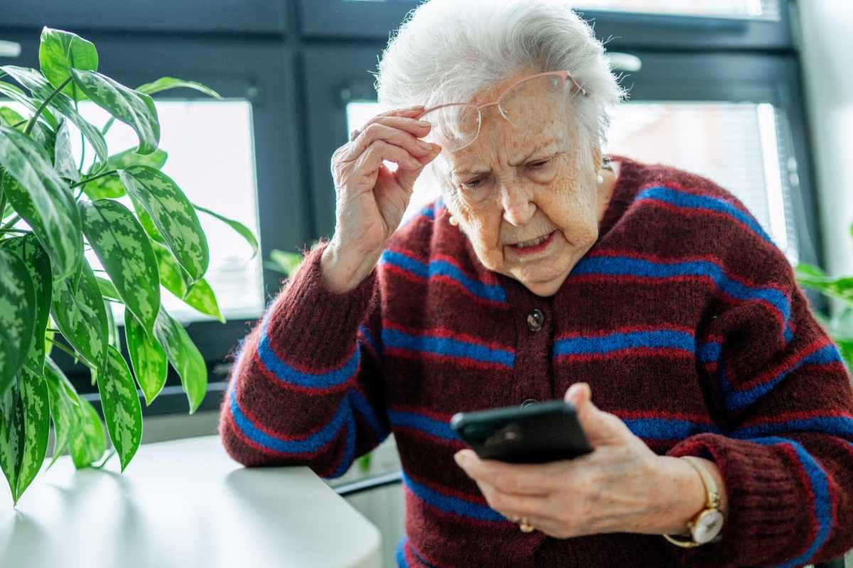 Donna anziana osserva con preoccupazione uno smartphone dopo aver ricevuto un SMS sospetto, immagine che rappresenta una possibile truffa digitale.