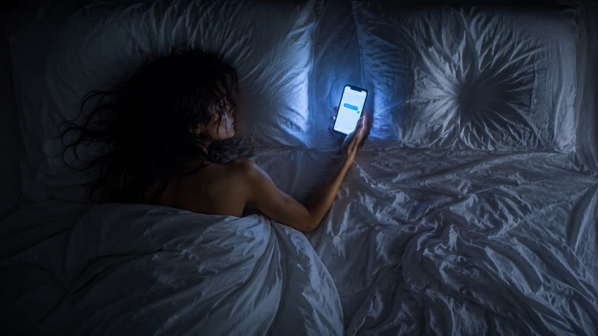 Donna distesa su un letto con smartphone in mano accanto a una metà del letto vuota, simbolo di una situationship e del burnout emotivo