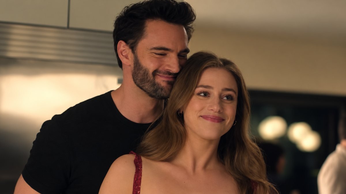Olive e Adam sorridono vicini in una scena di The Love Hypothesis, con luci calde sullo sfondo.